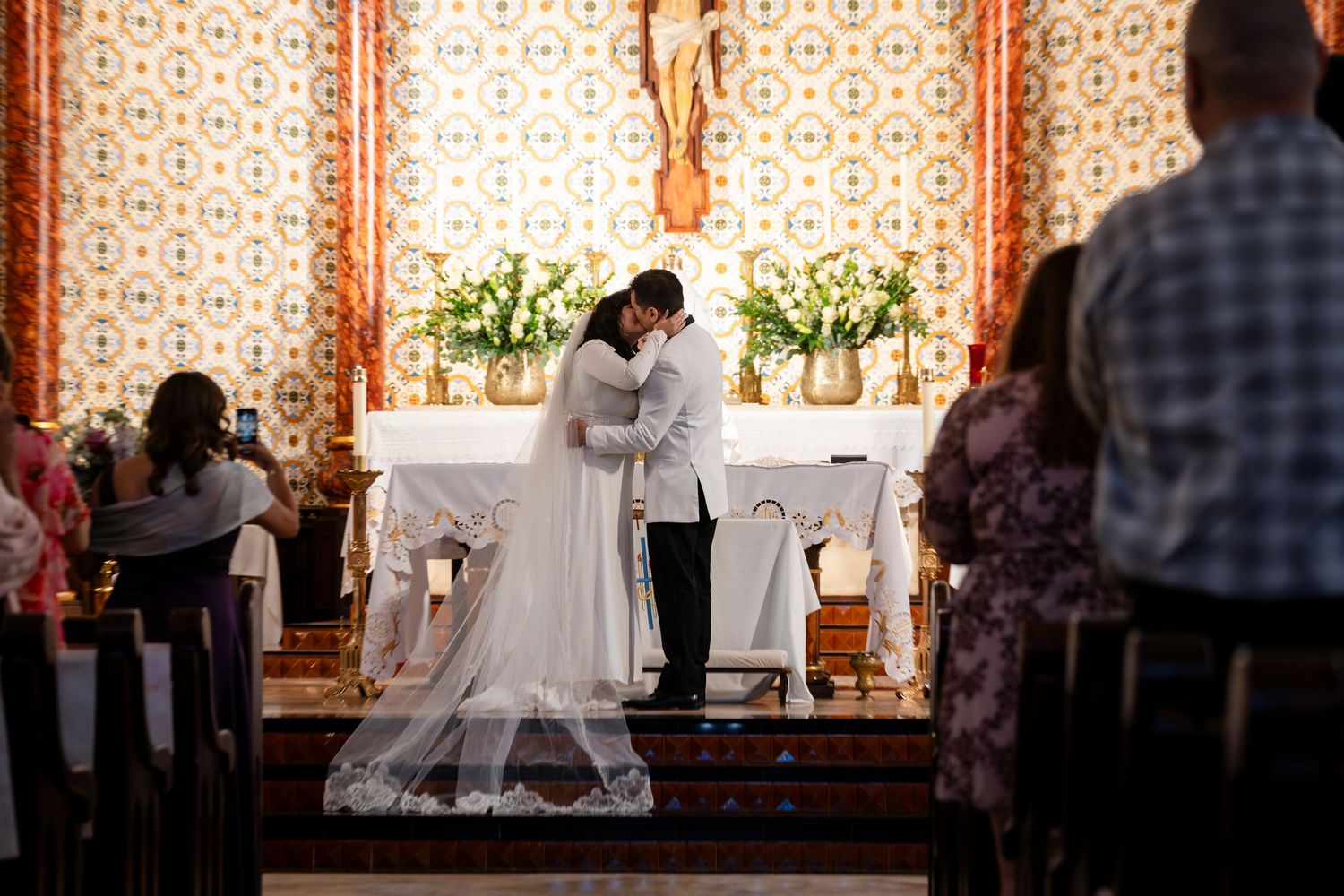 A couple shares an intimate moment at the altar during their church wedding ceremony with a cathedral veil flowing behind.