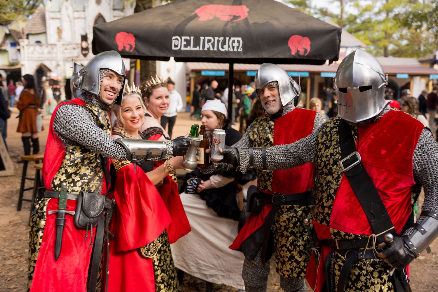 Medieval knights in red and gold costumes performing a choreographed sword fight at a Renaissance faire.