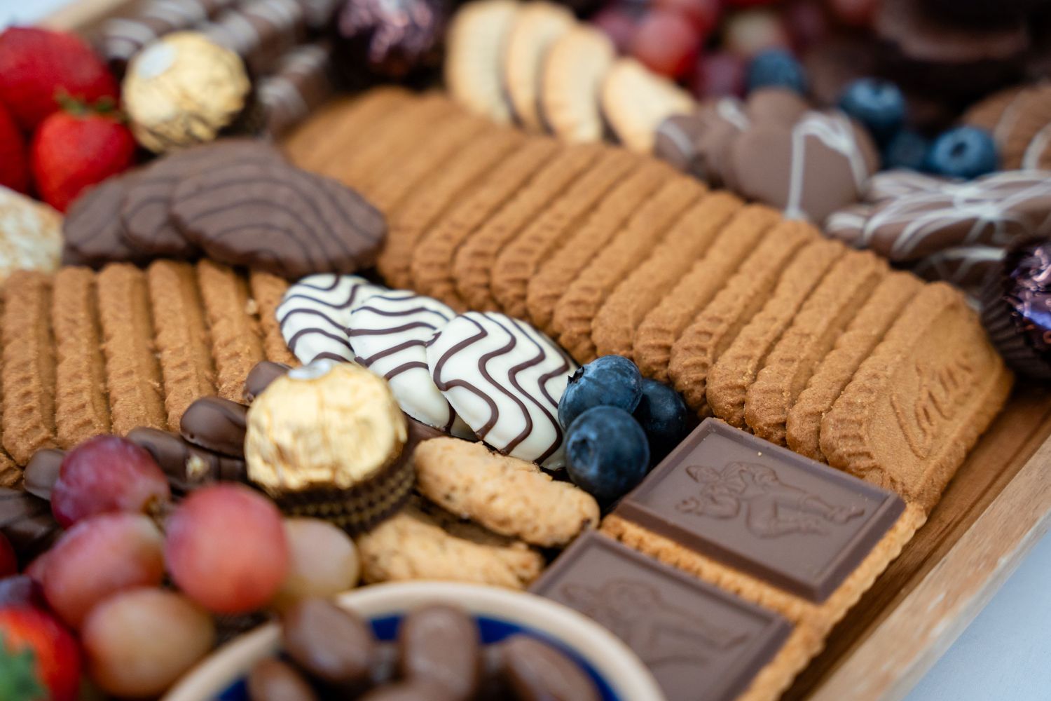 Close-up of gourmet cookies, chocolates and berries arranged on wooden serving board.