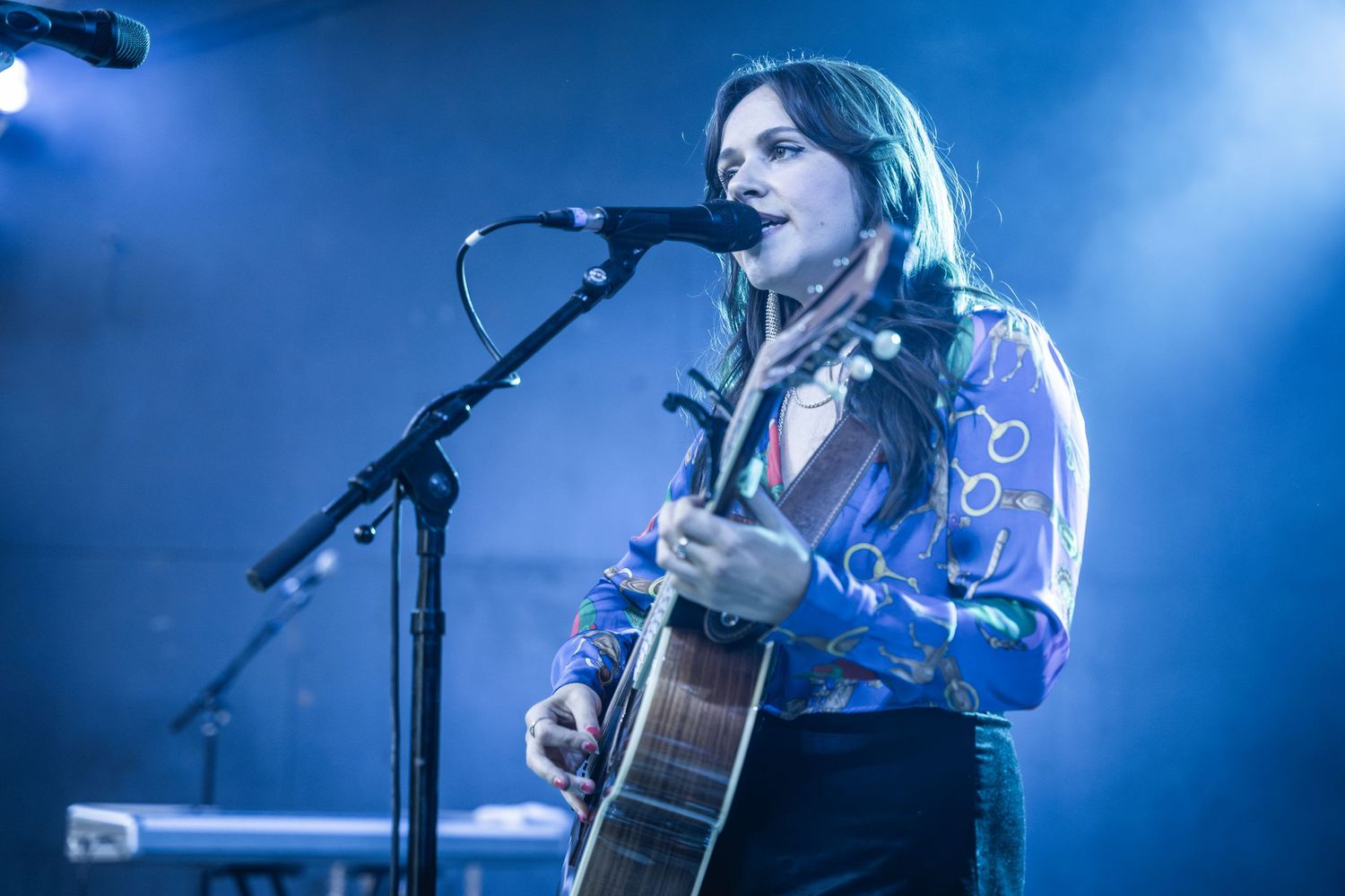 Concert performance with musician playing acoustic guitar under dramatic blue stage lighting.