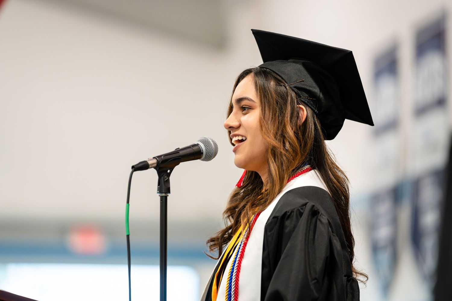 Graduate in cap and gown performing at microphone during ceremony.