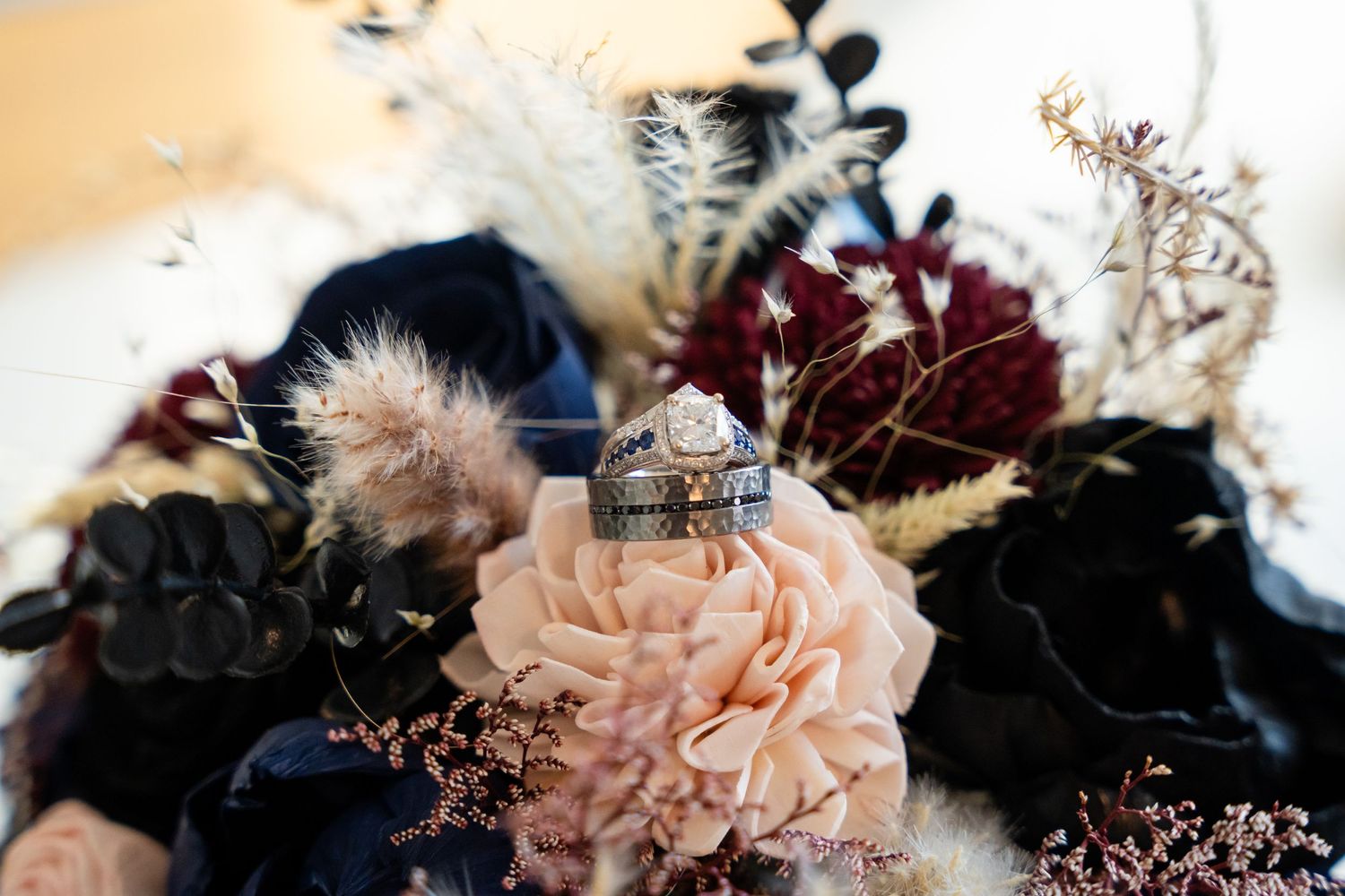 Wedding rings displayed artistically on pink and burgundy florals with dark accents.