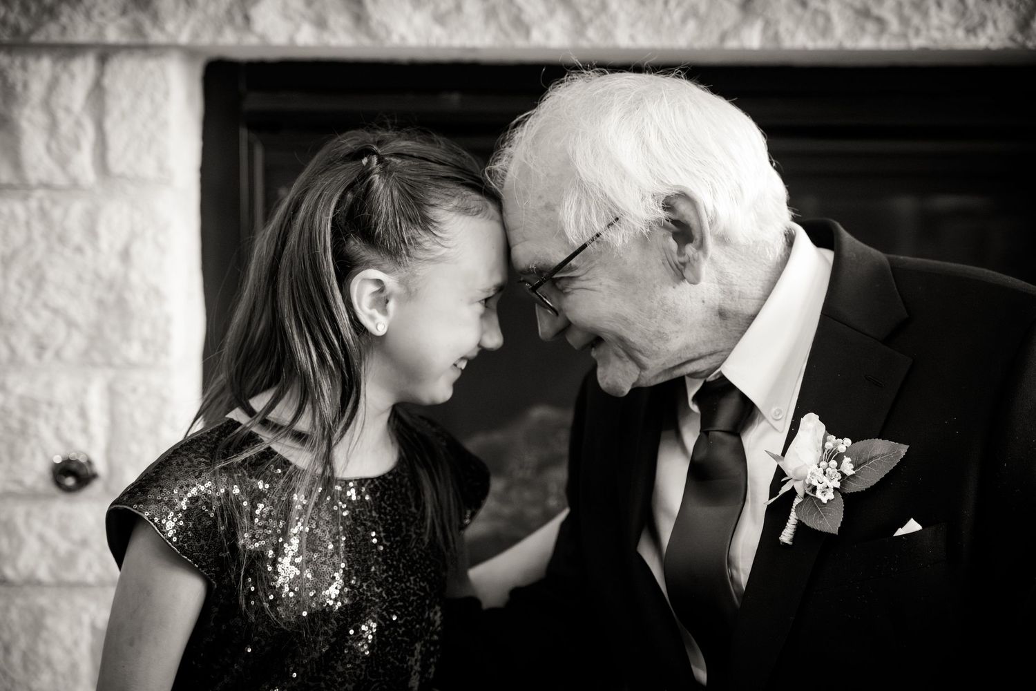 A tender moment in black and white as a young girl and elderly man in a suit share a touching forehead embrace.