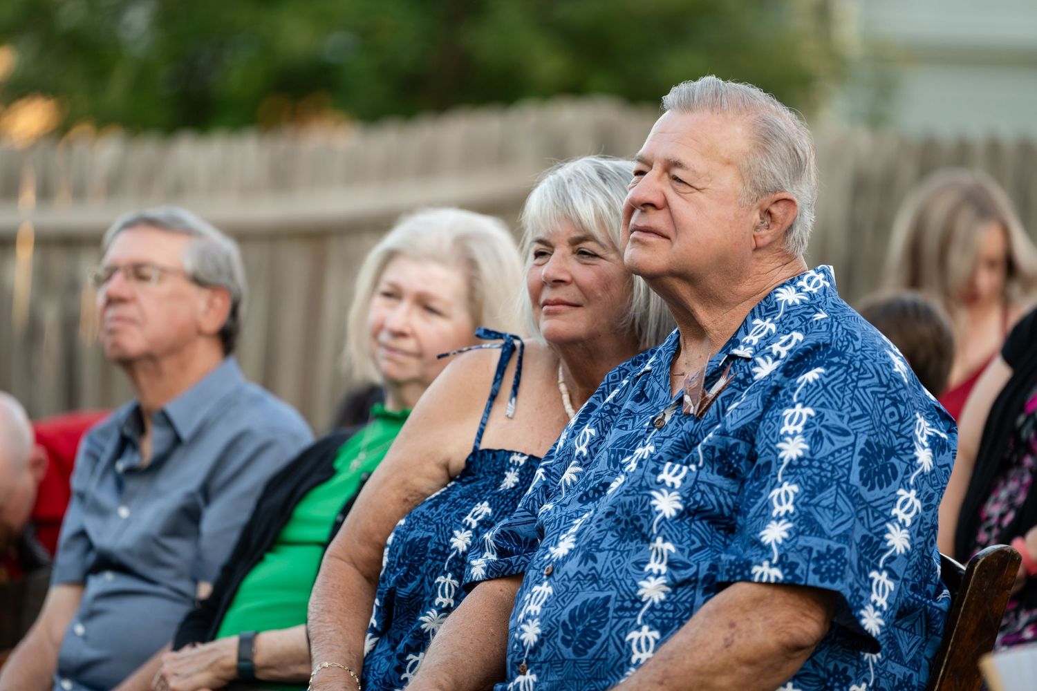 Wedding guests in blue Hawaiian shirts watch ceremony from outdoor seating area.
