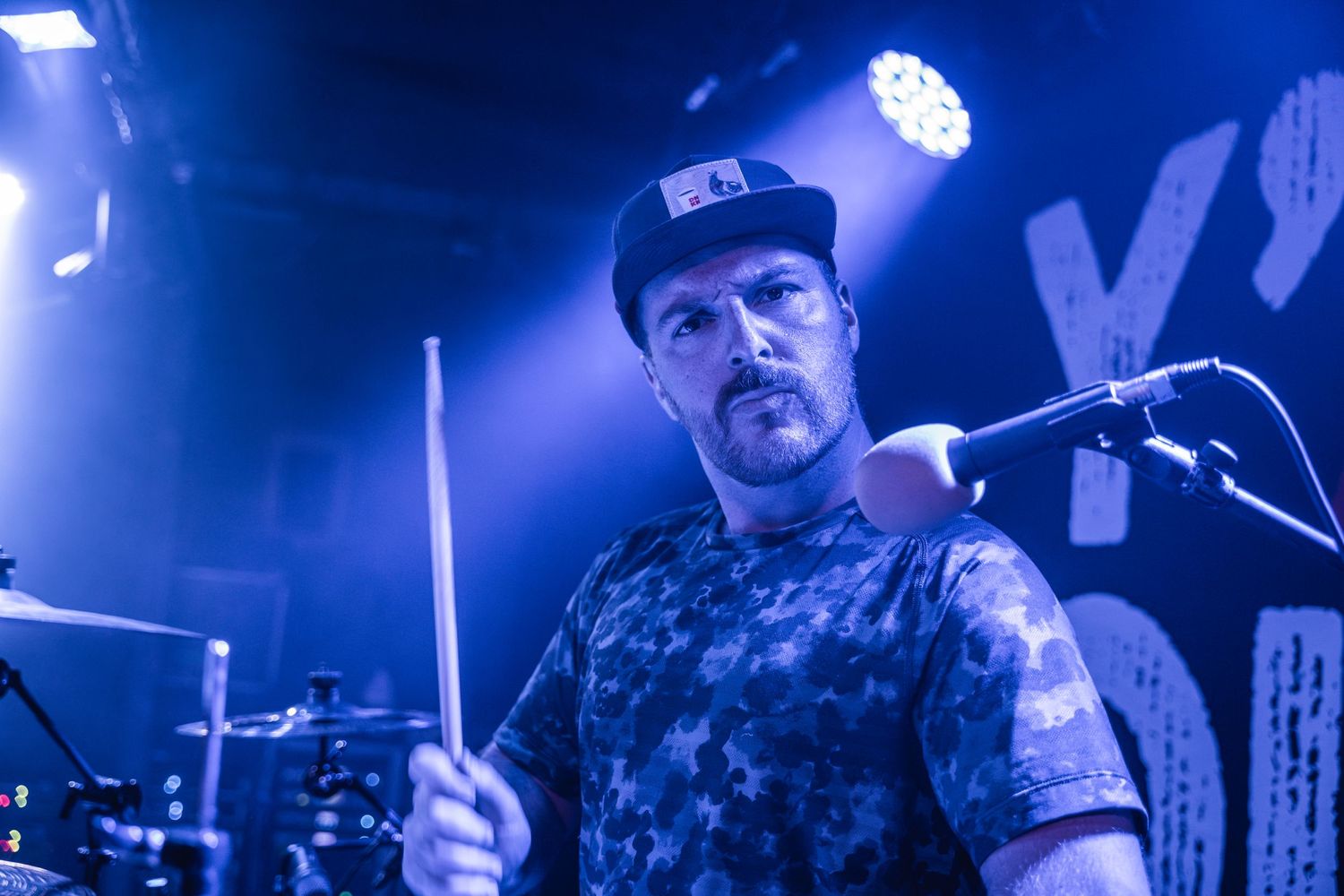 Concert drummer playing with intense concentration under blue stage lights.