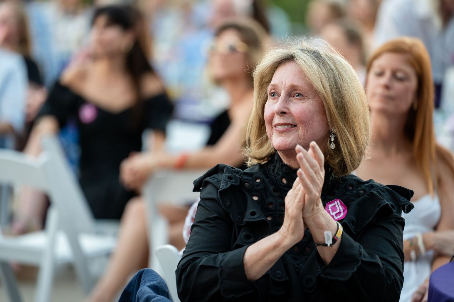 Audience member in black ruffled top emotionally engaging with event presentation.