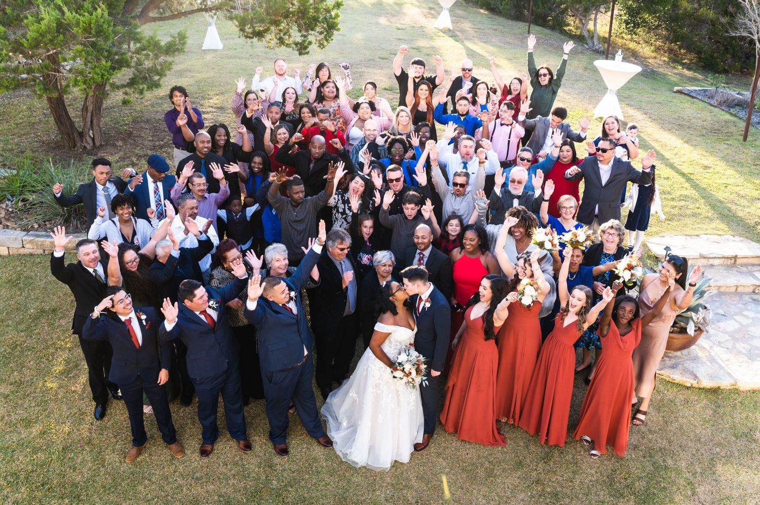 Cheerful wedding party poses for a fun group photo outdoors with bridesmaids in rust-colored gowns.