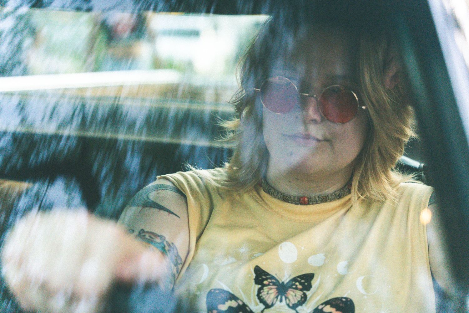 Dreamy portrait through car window showing person in yellow shirt with butterfly design.