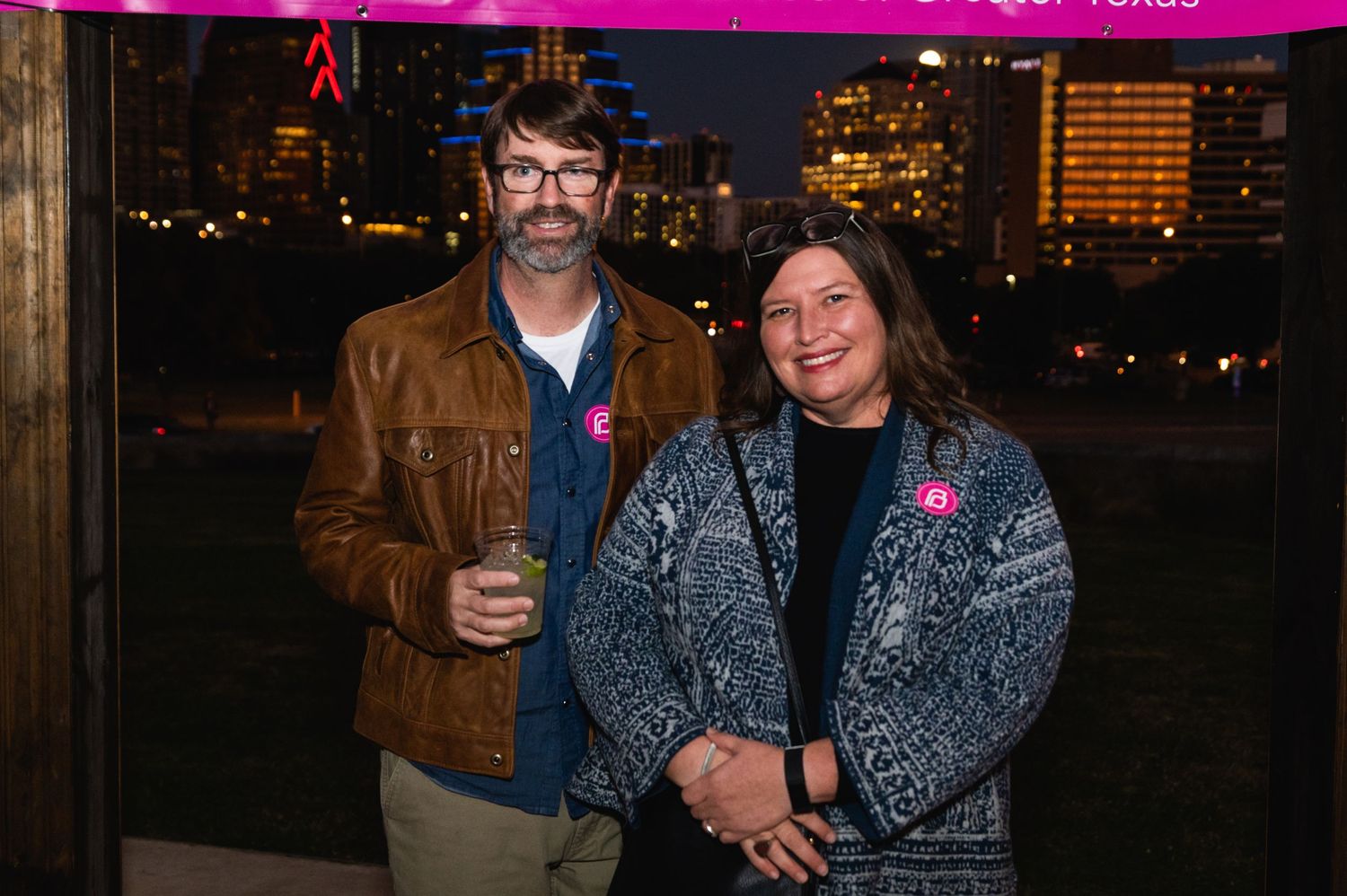 Couple poses under pink lighting at nighttime outdoor event.