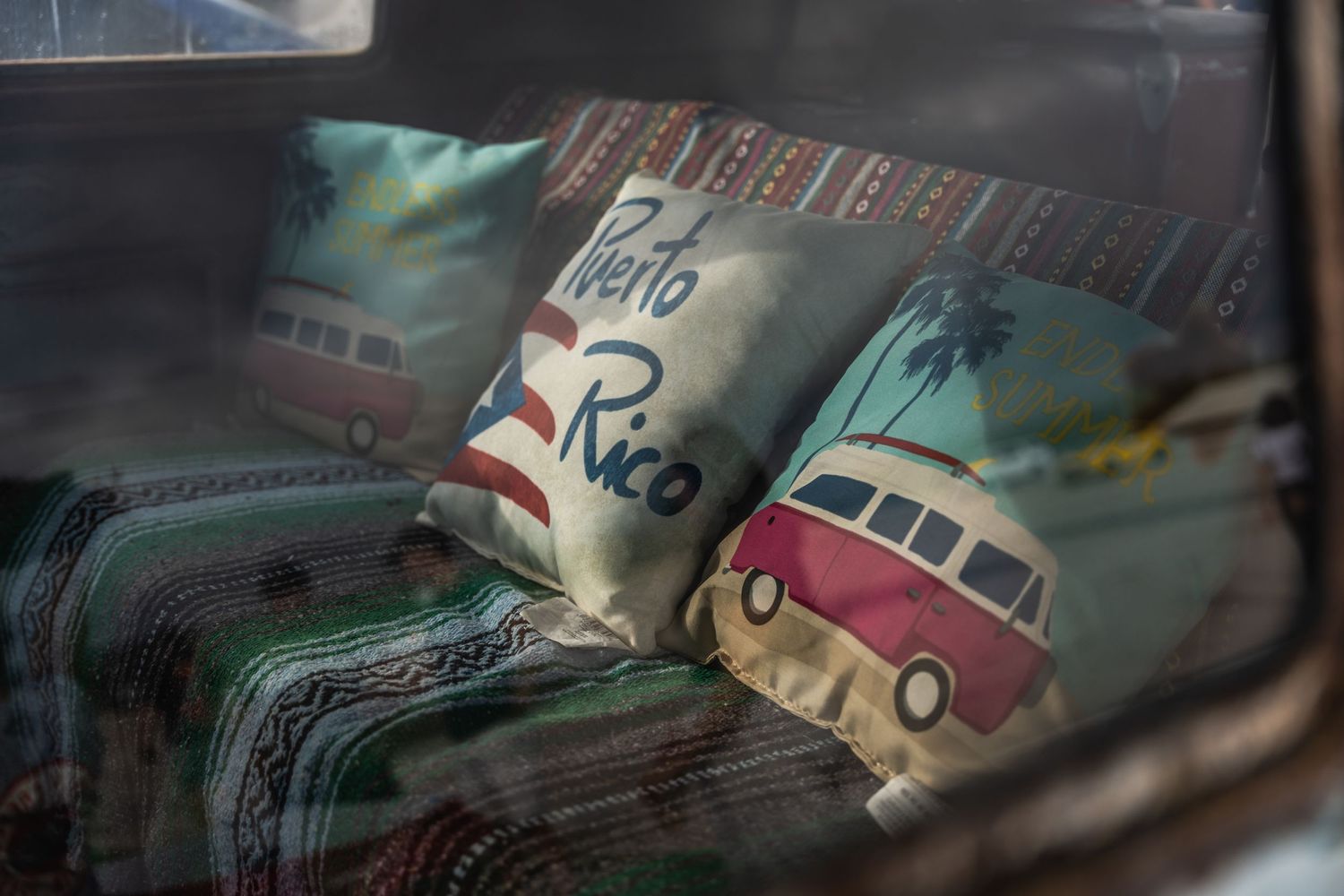 Vintage VW bus themed decorative pillows visible through a car window.