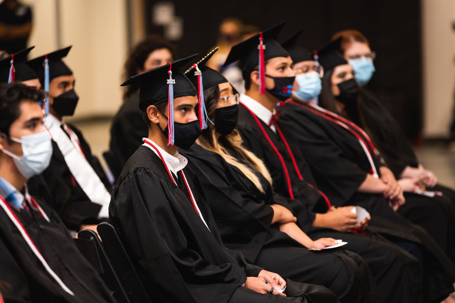 College graduates in black robes and masks attend a formal graduation ceremony.