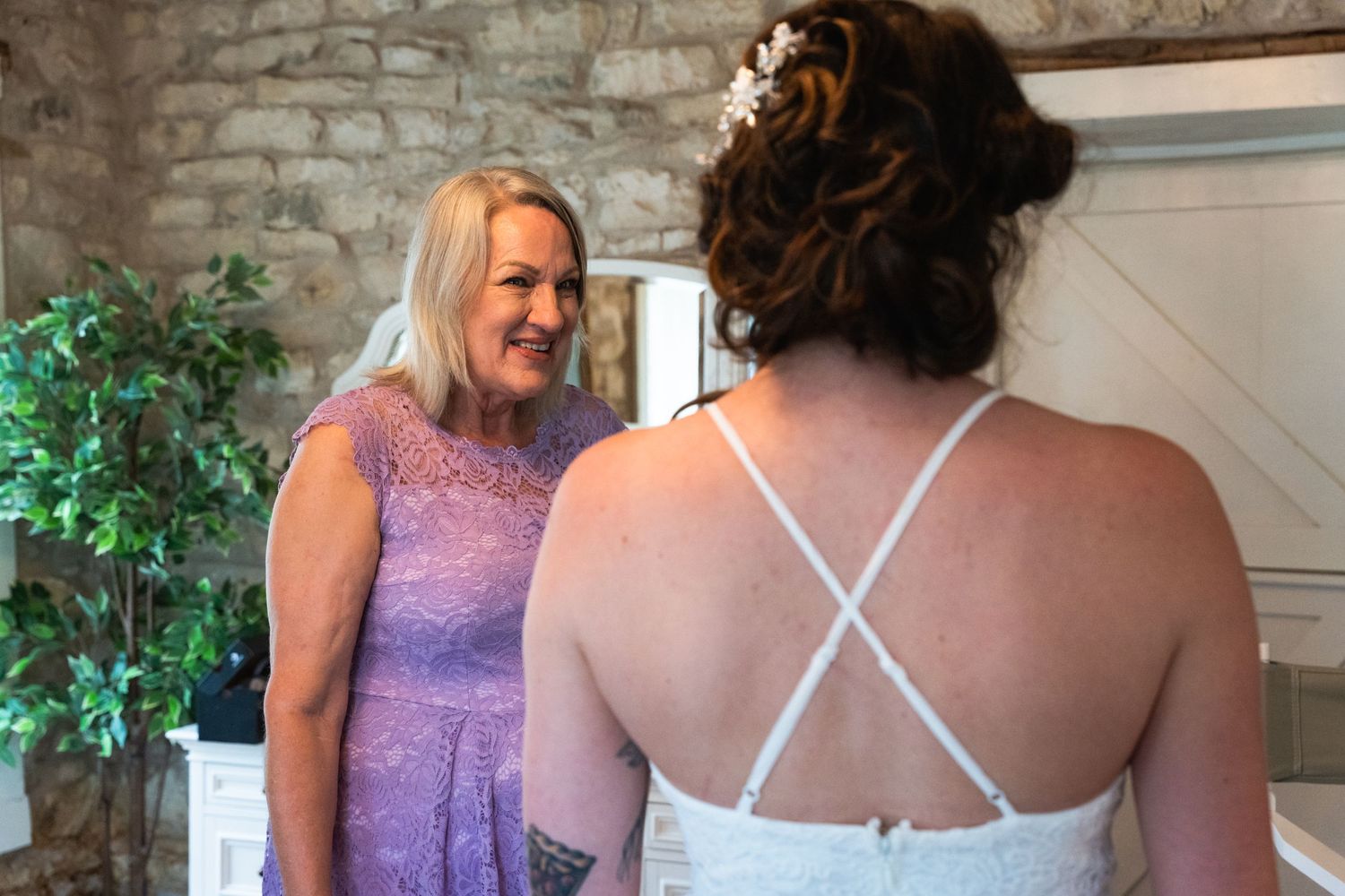Two women in formal dresses share a moment in an elegant stone-walled room.