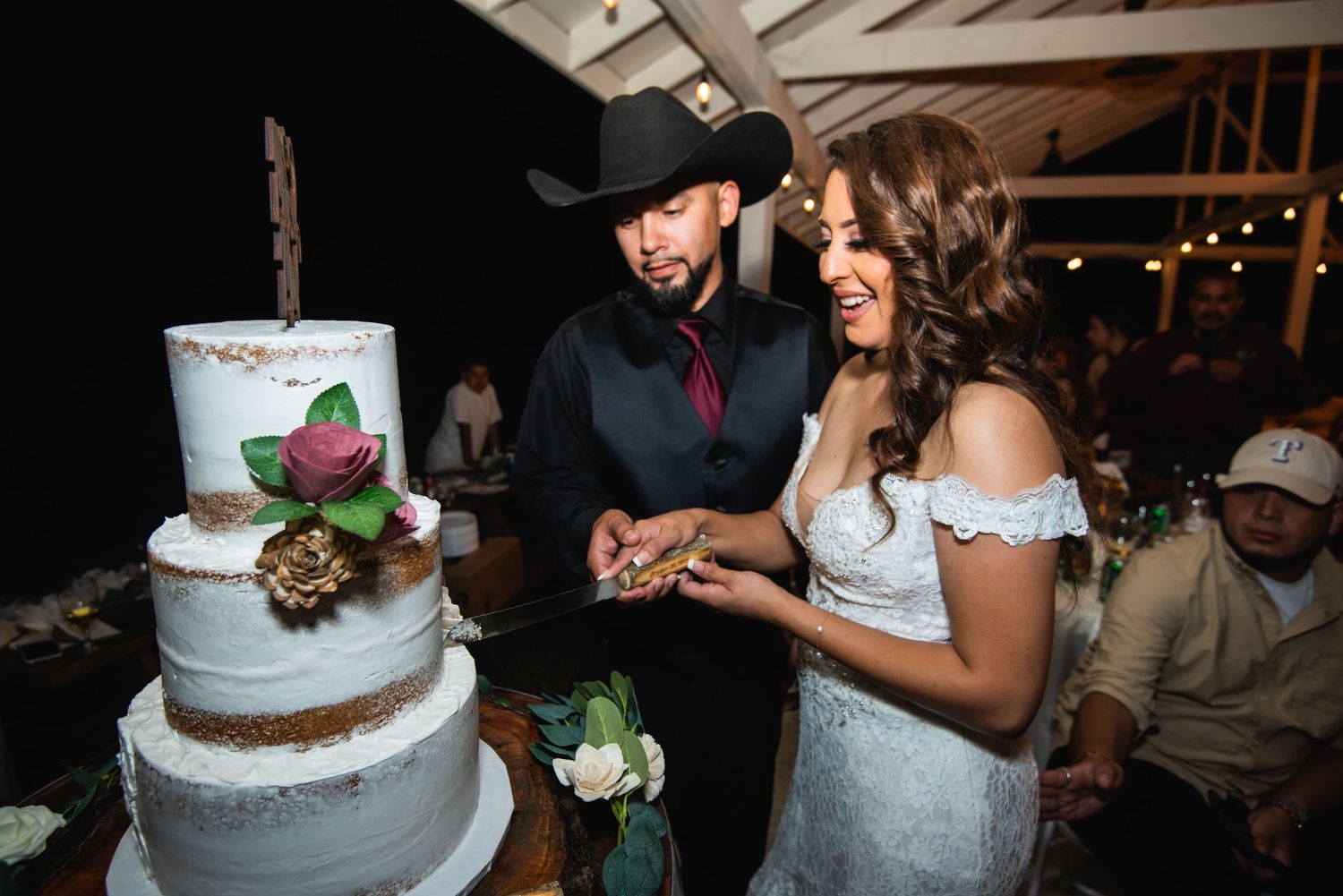 A couple cuts their elegant three-tier wedding cake decorated with floral accents.
