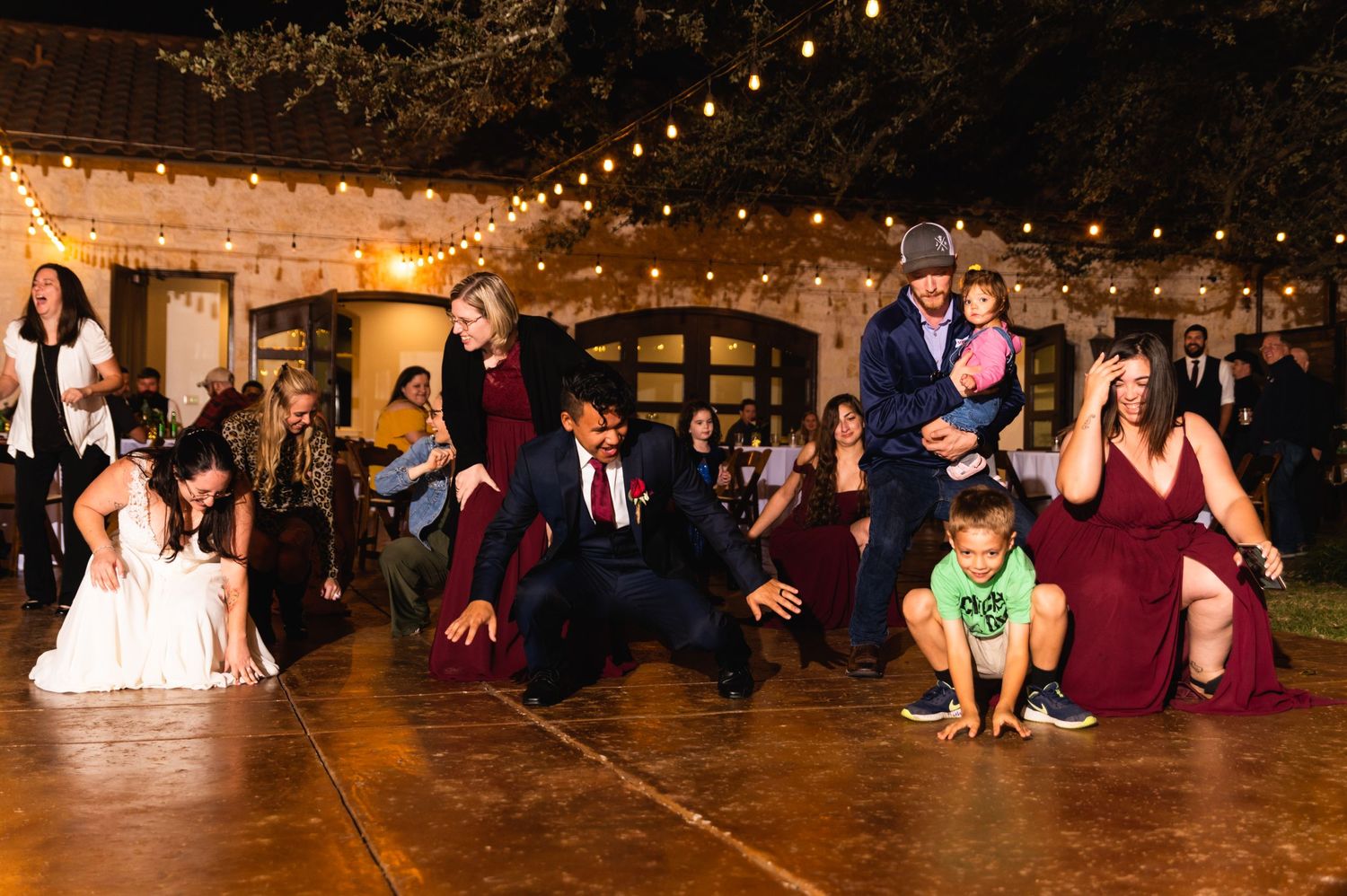 Energetic group dance moment at a wedding reception with string lights overhead.