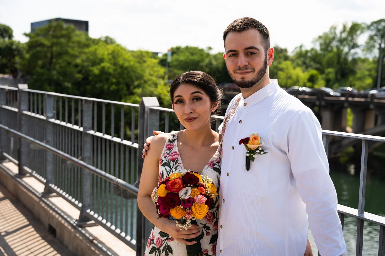 A couple poses together on an outdoor deck wearing formal attire with fall-colored floral accents.