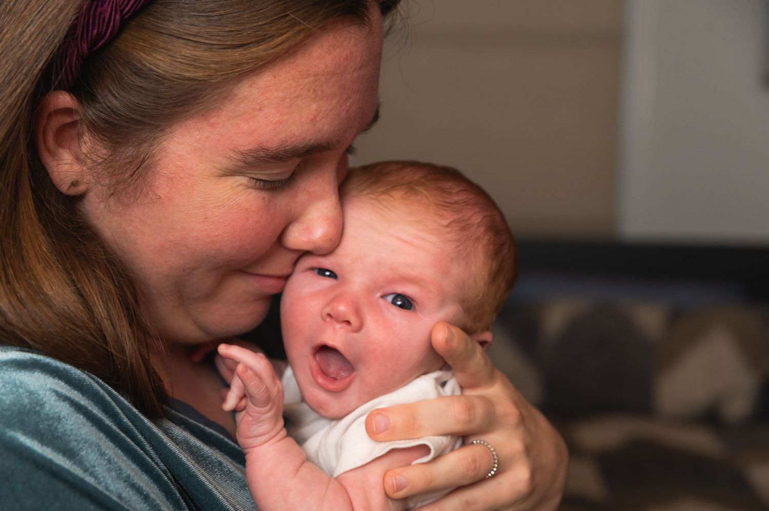 Mother holds yawning baby in casual indoor setting.