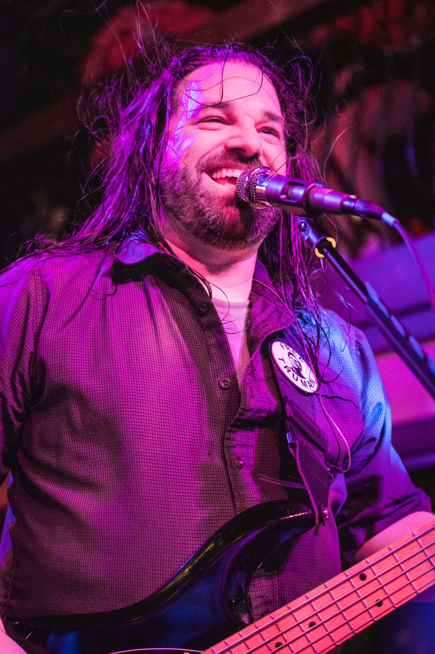 Bass player with long hair performs under purple stage lighting.