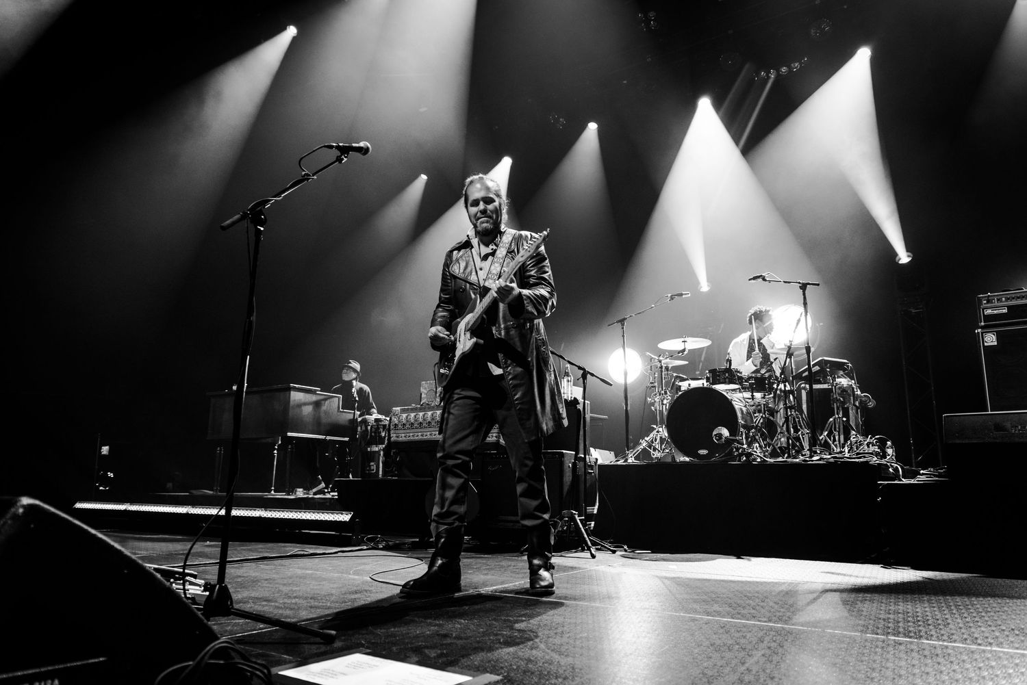 Black and white concert photo of performer playing guitar on dramatically lit stage.