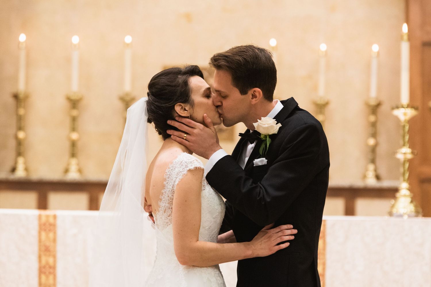Romantic wedding kiss moment with lit candles in church altar background.