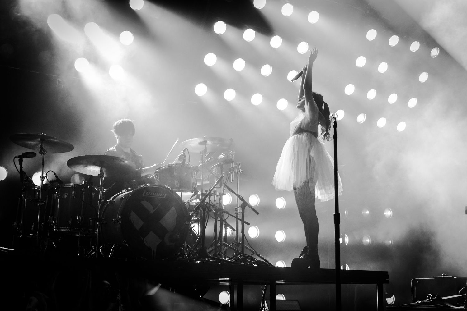 Black and white concert photo showing a dramatic silhouette against bright stage lighting.