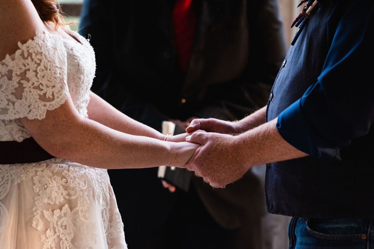 Close-up of hands joining together during wedding ring exchange ceremony.