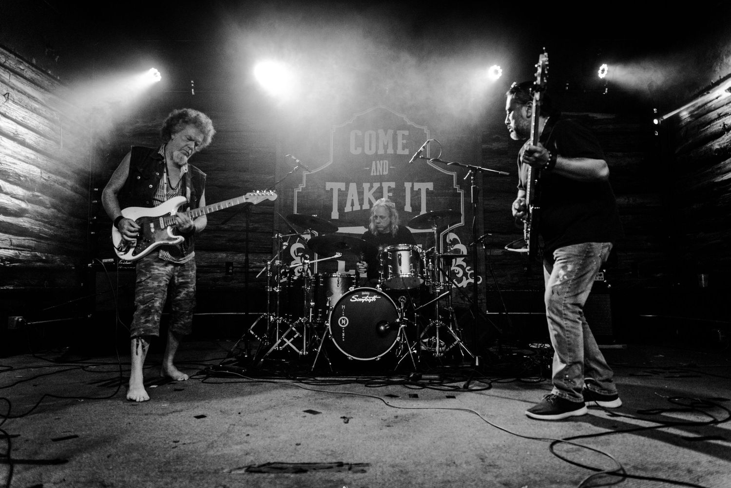 Band performs on stage with drum kit and guitars visible under 'Take It' sign.