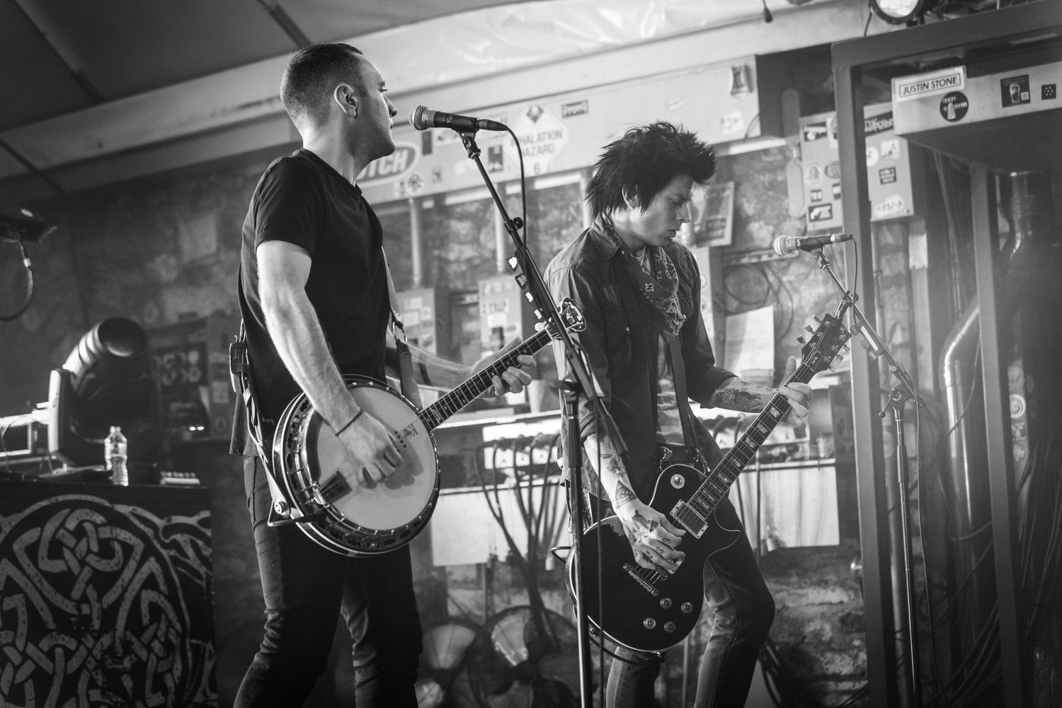 Black and white photo of musicians playing guitar and bass during an intimate venue performance.