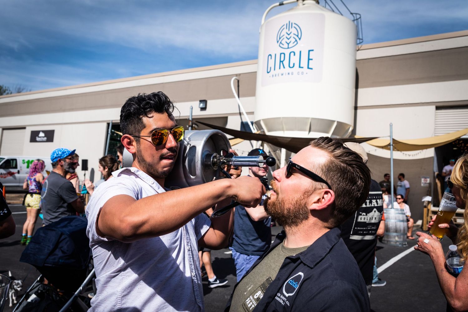 Two people interact with beer kegs at Circle Brewing Company's outdoor event.