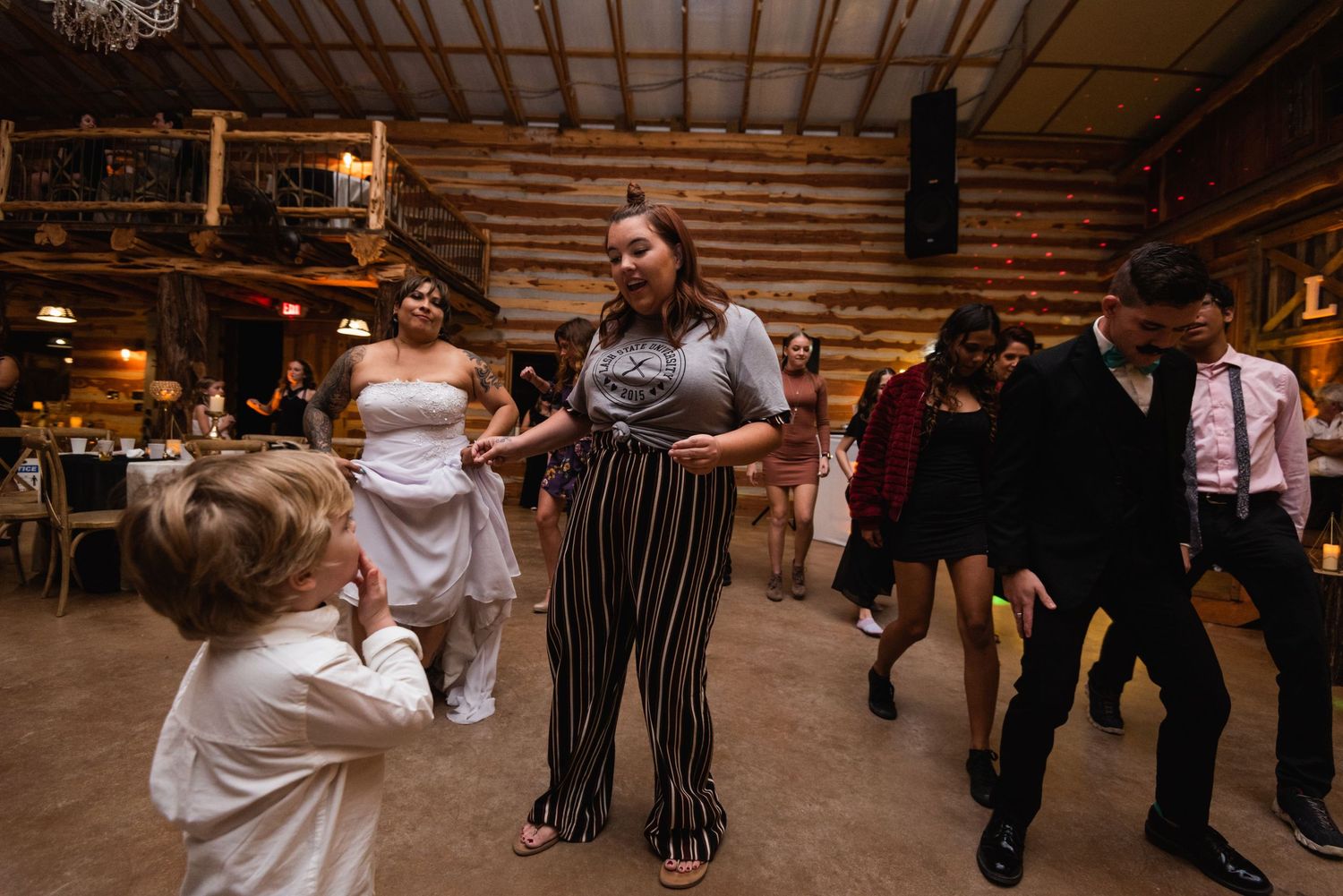 Wedding guests dance and celebrate on the dance floor at a rustic barn reception.