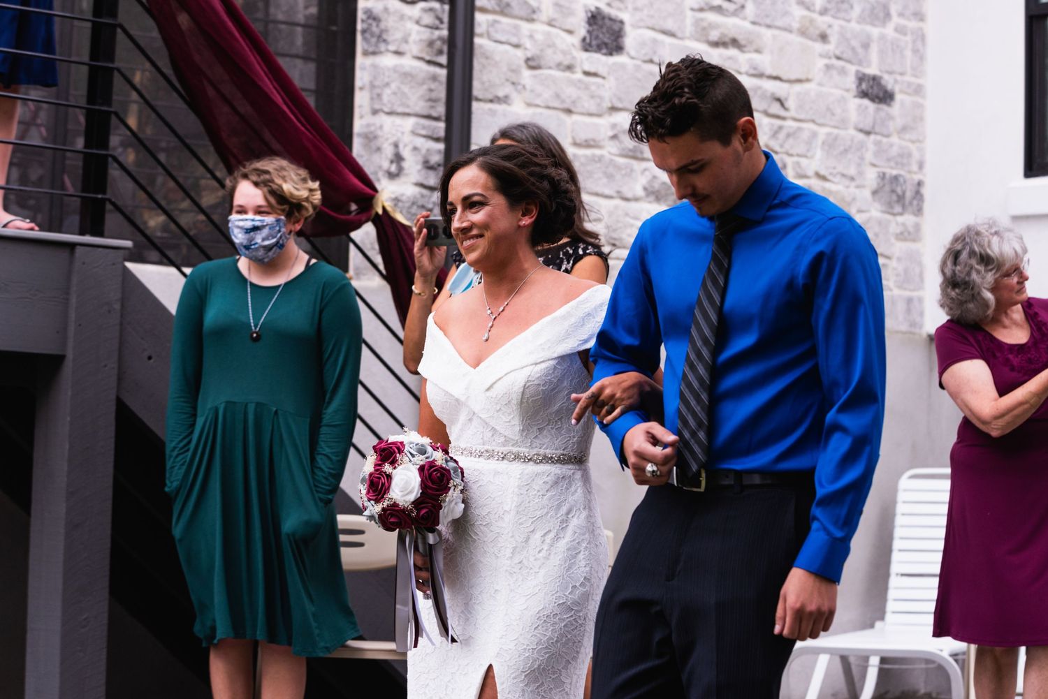 Wedding party members in colorful attire walking outside brick building.
