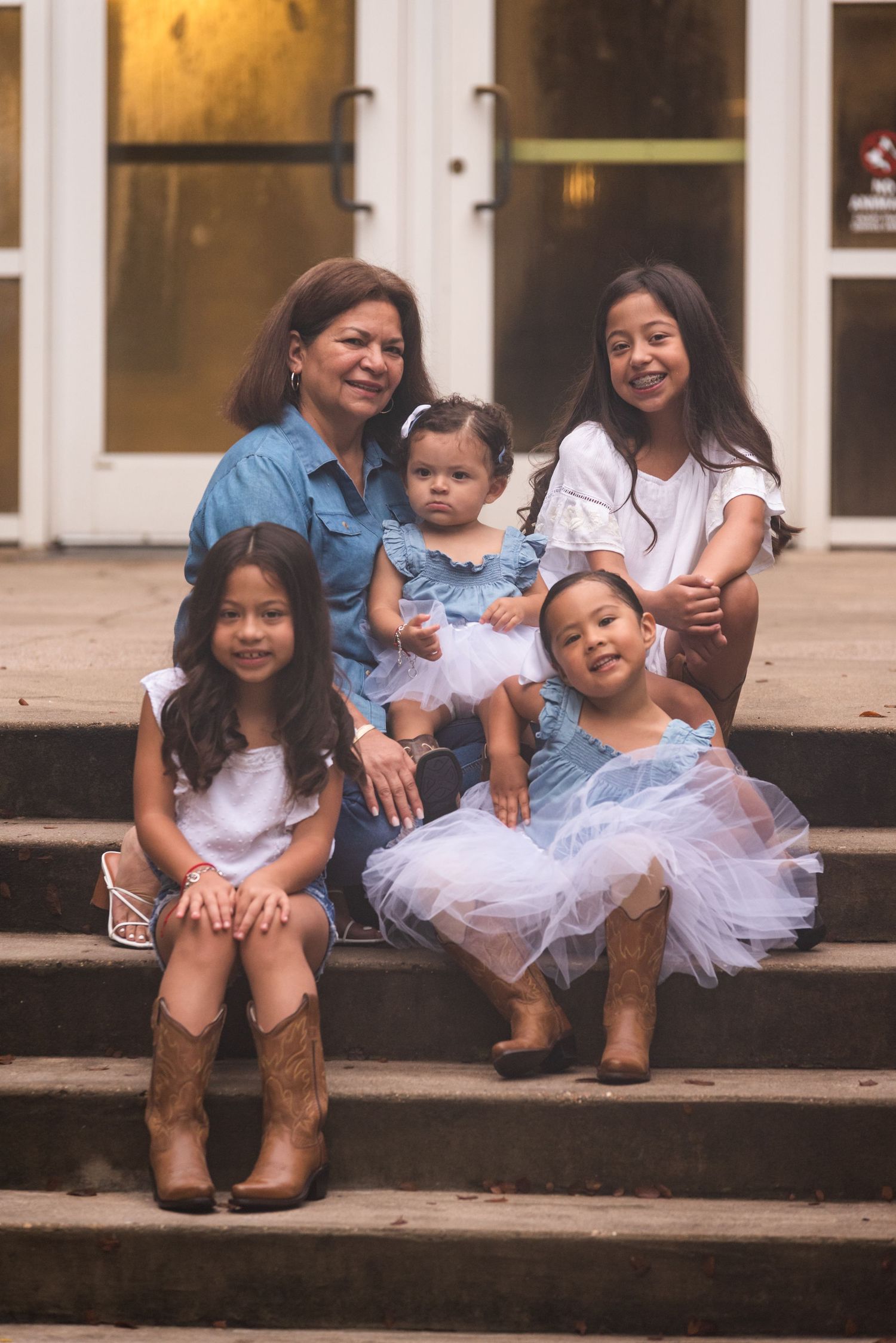 A multi-generational family portrait on stone steps wearing matching casual outfits in blue and white.