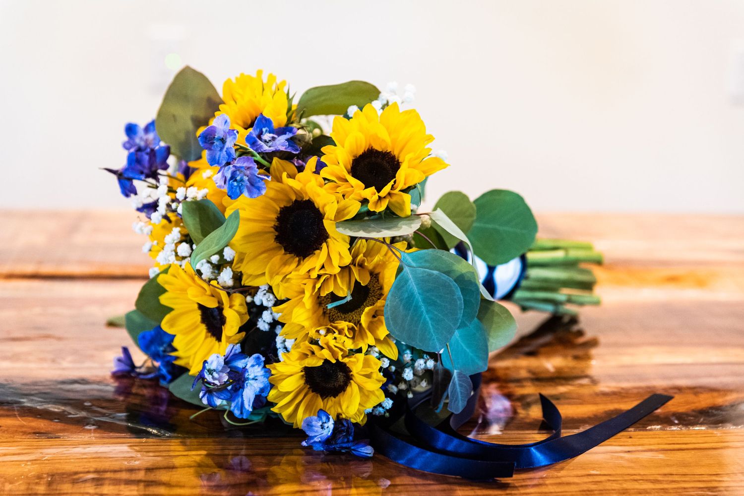 Vibrant sunflower and blue flower bouquet on a wooden surface.