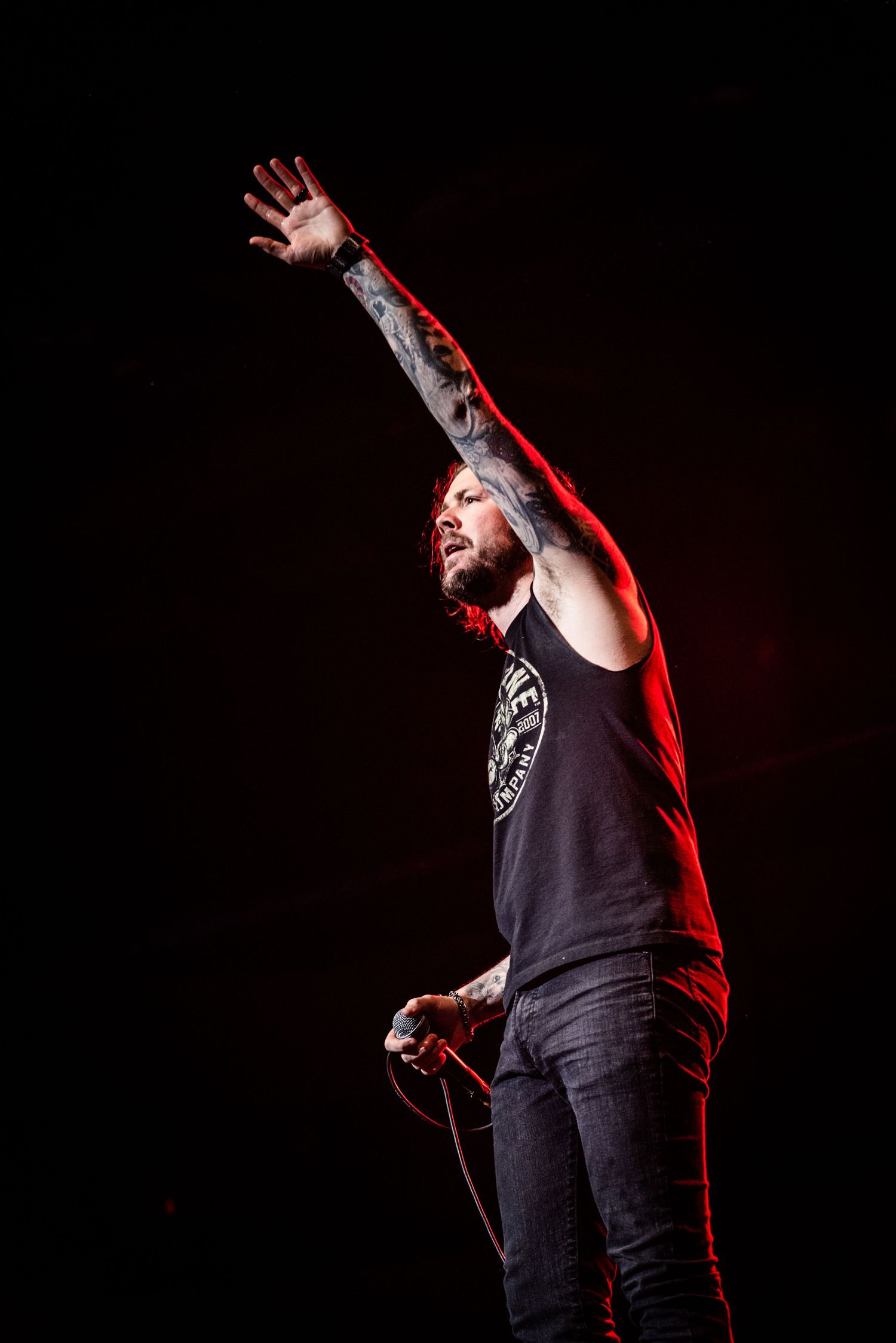 A performer raises their tattooed arm during an emotional concert performance.