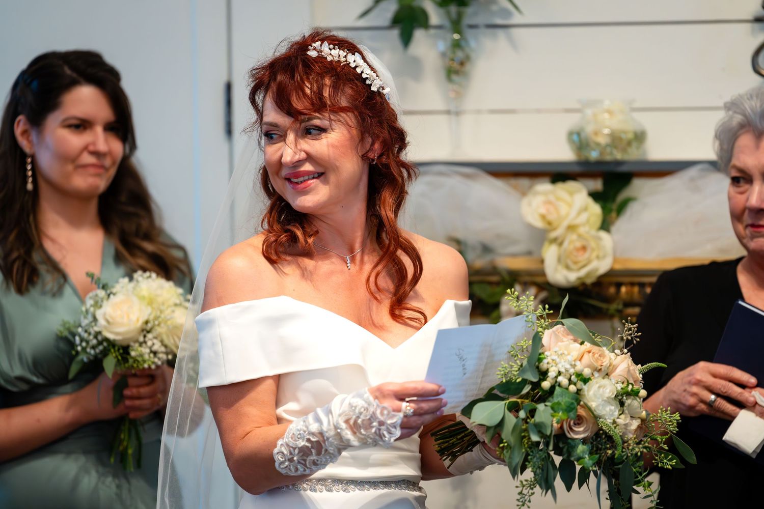 A bride in an off-shoulder wedding dress holds a bouquet of white flowers at a wedding ceremony.