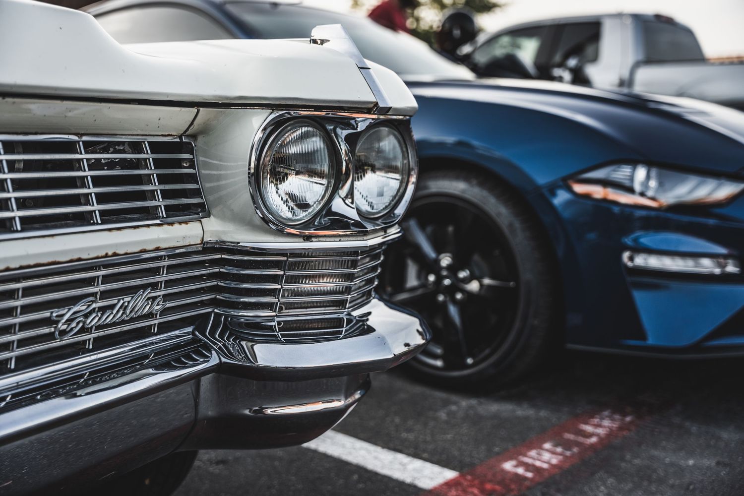Close-up detail of classic car headlights and chrome grille with modern sports car in background.