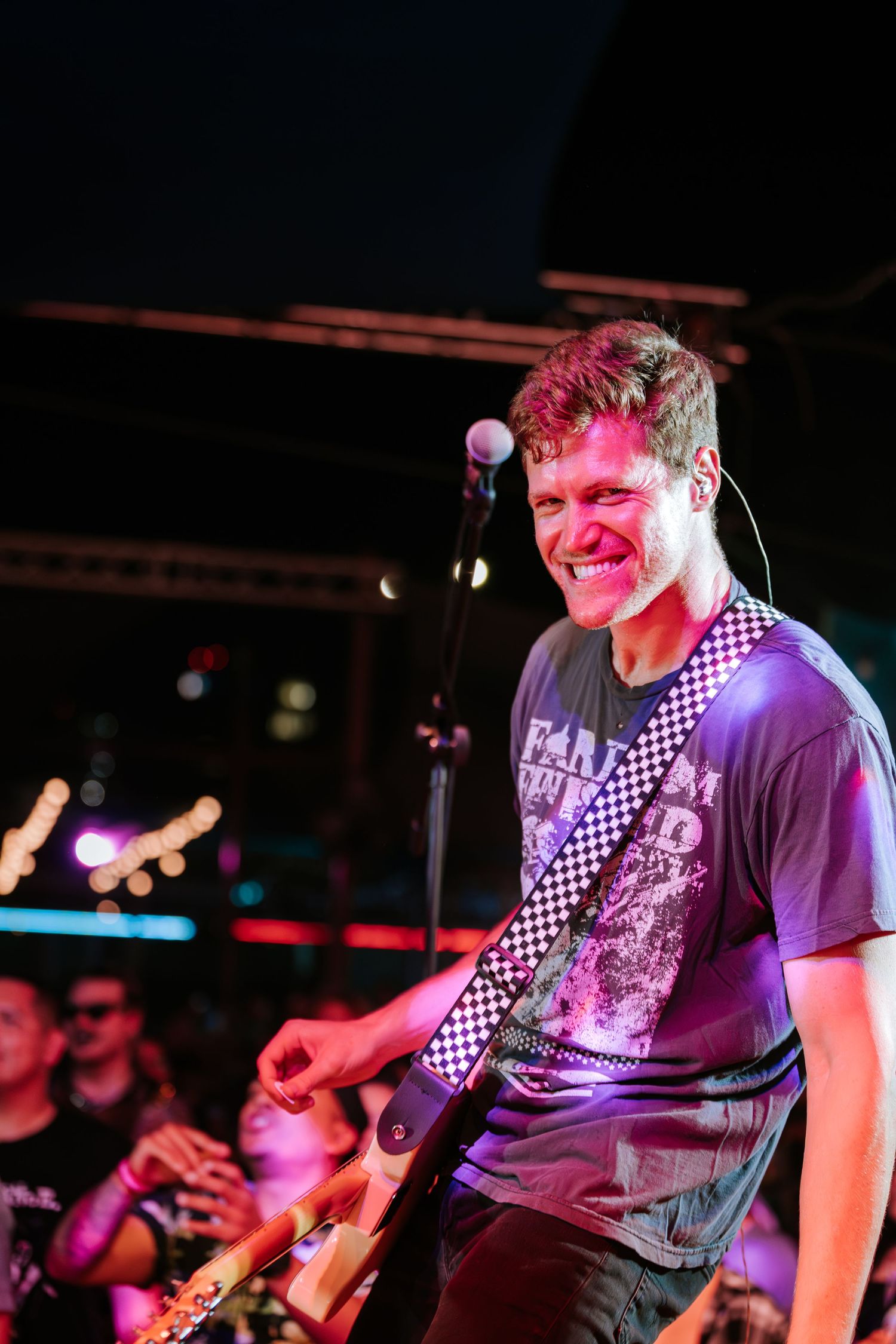 Musician smiling while performing under pink stage lights at concert venue.