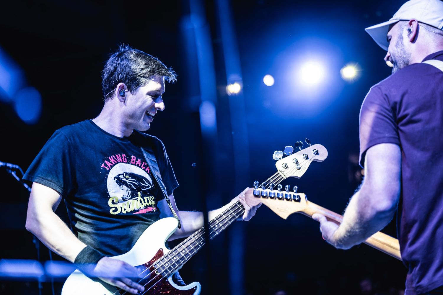 Musicians playing bass and guitar on stage illuminated by blue spotlights.