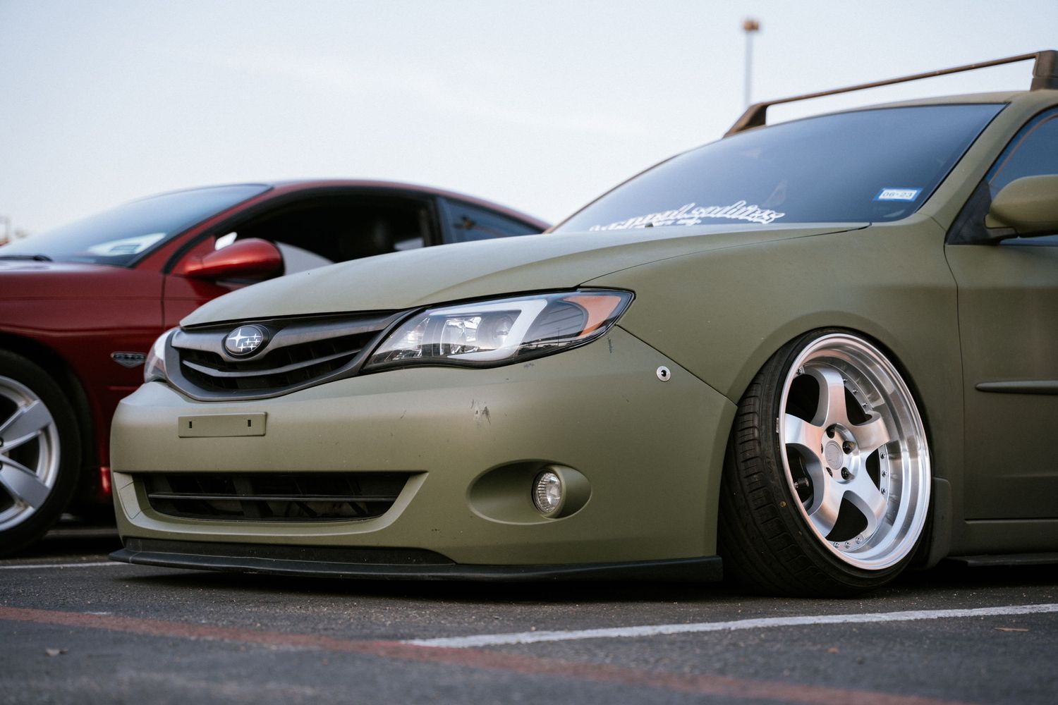 Modified olive green Subaru with lowered suspension and custom wheels parked at a car meet.