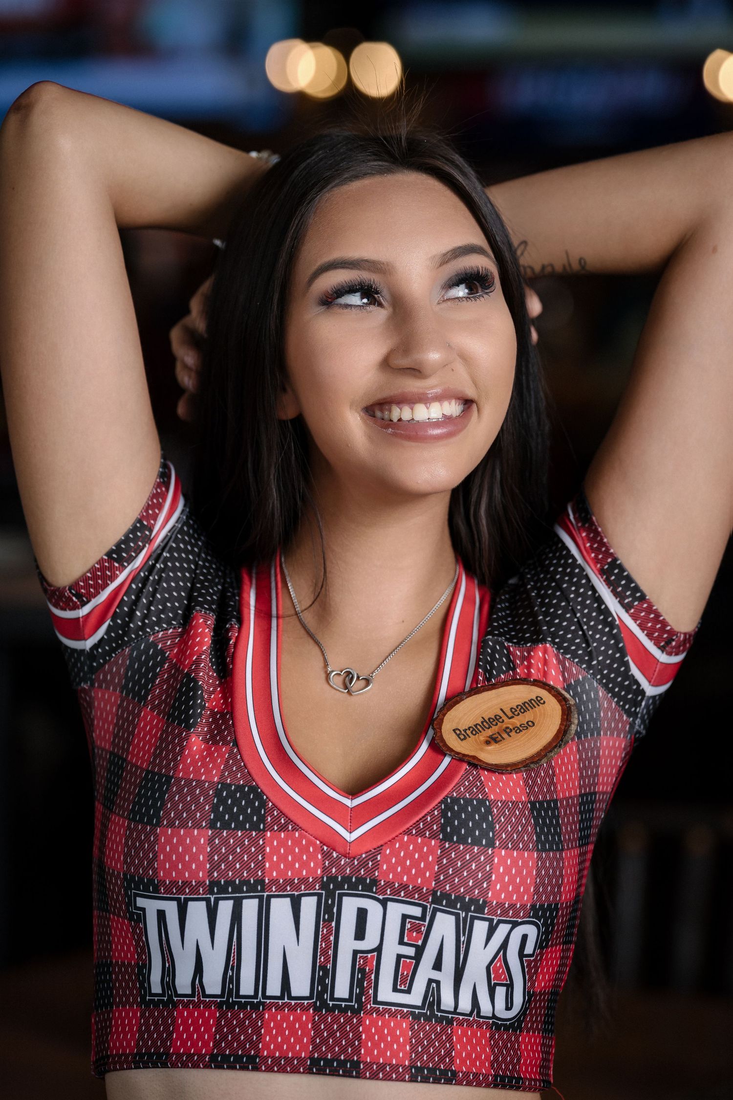 Sports bar server posing in buffalo plaid Twin Peaks uniform with arms raised.