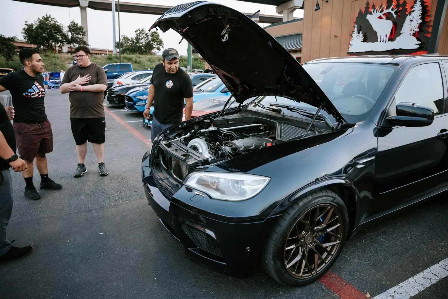 Black BMW with hood open being inspected at a car meet.