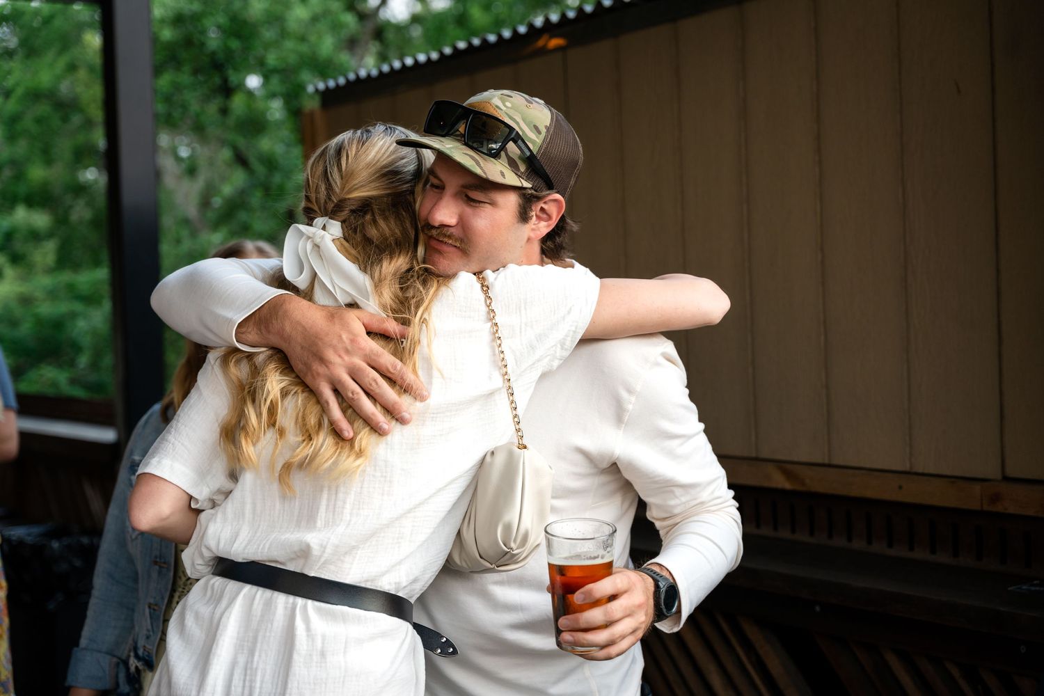 Two people sharing embrace at outdoor celebration while holding drinks.