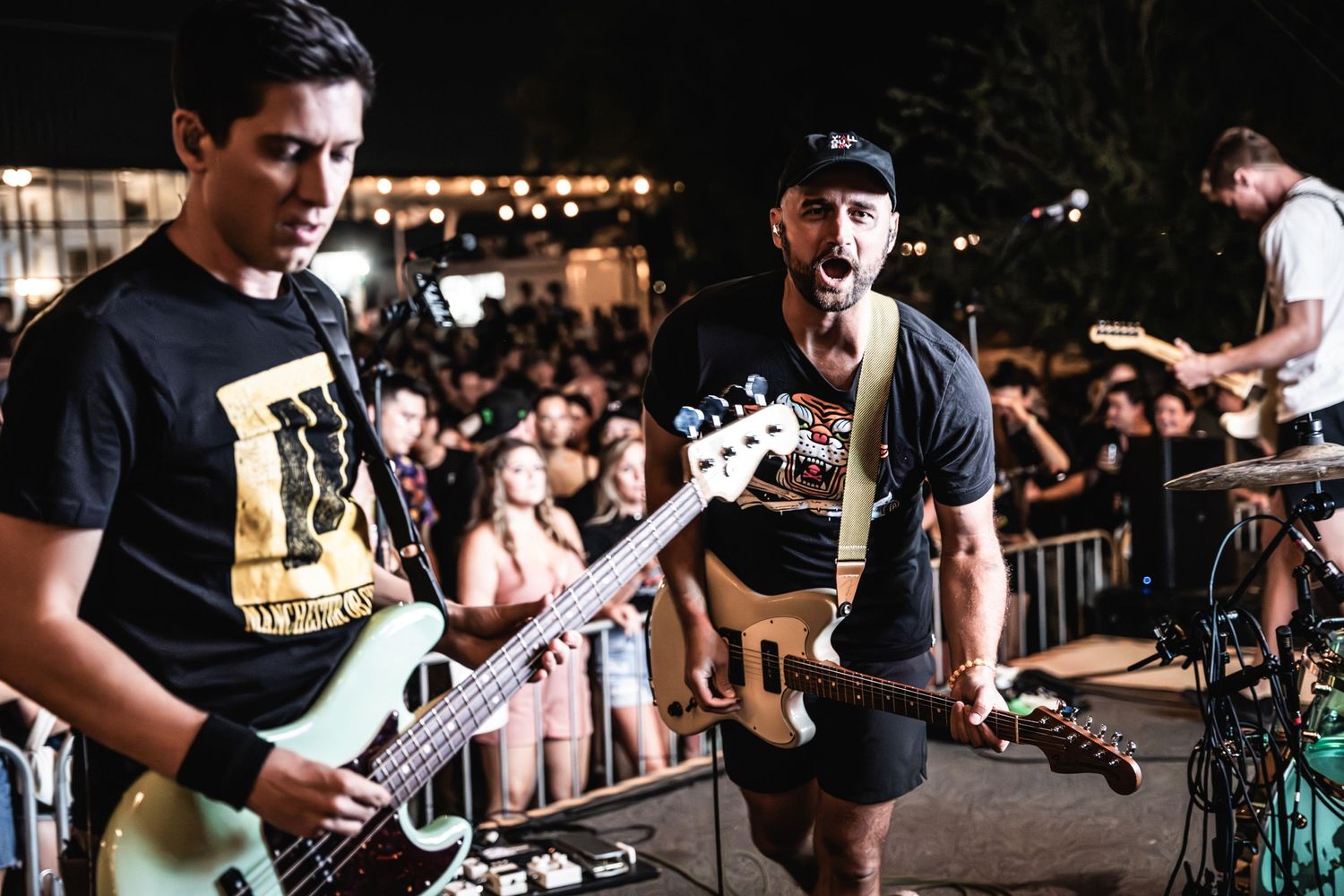 Two musicians perform on stage with guitars at an outdoor concert.