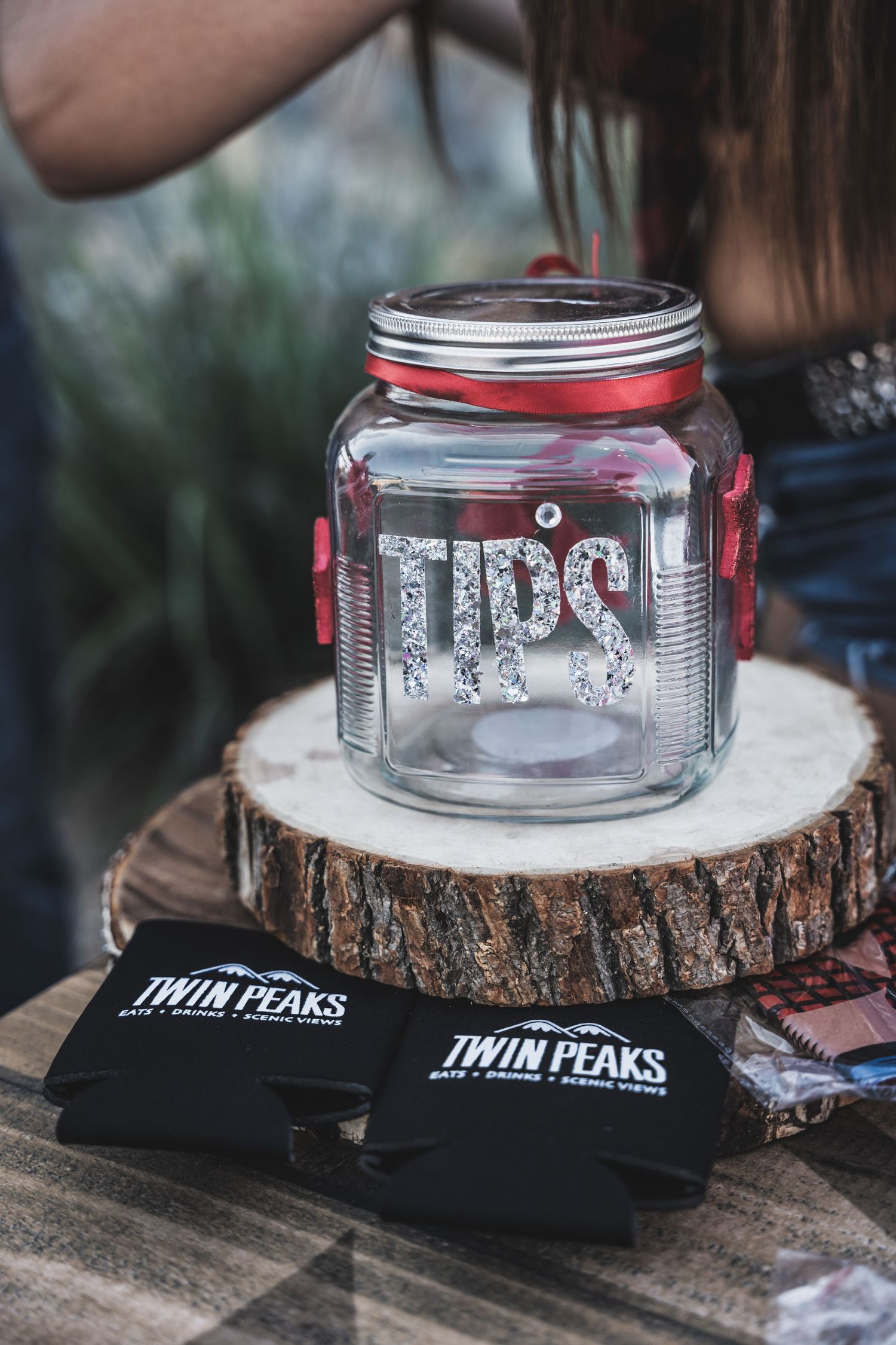 Glass tip jar on wooden log slice with Twin Peaks branded koozies.