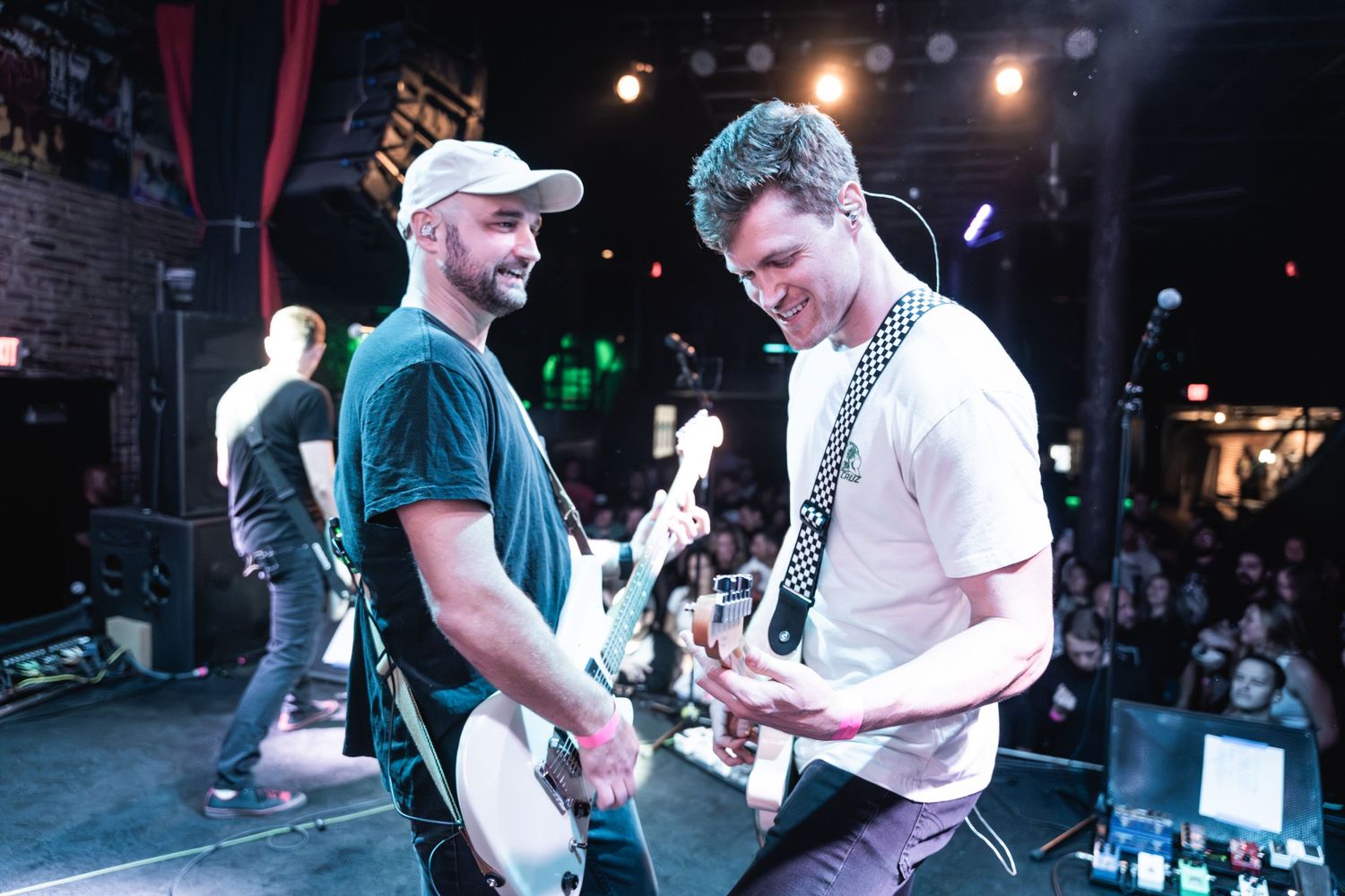 Musicians sharing a lighthearted moment while playing guitars during live performance.