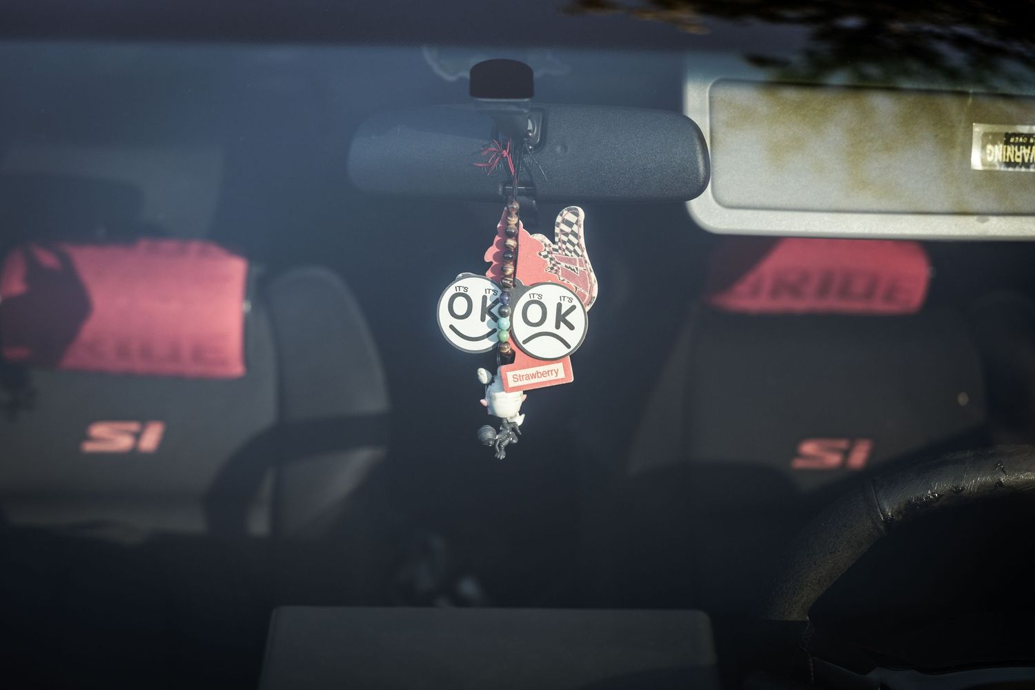 Cute cartoon air freshener hanging from a rearview mirror in a car interior.