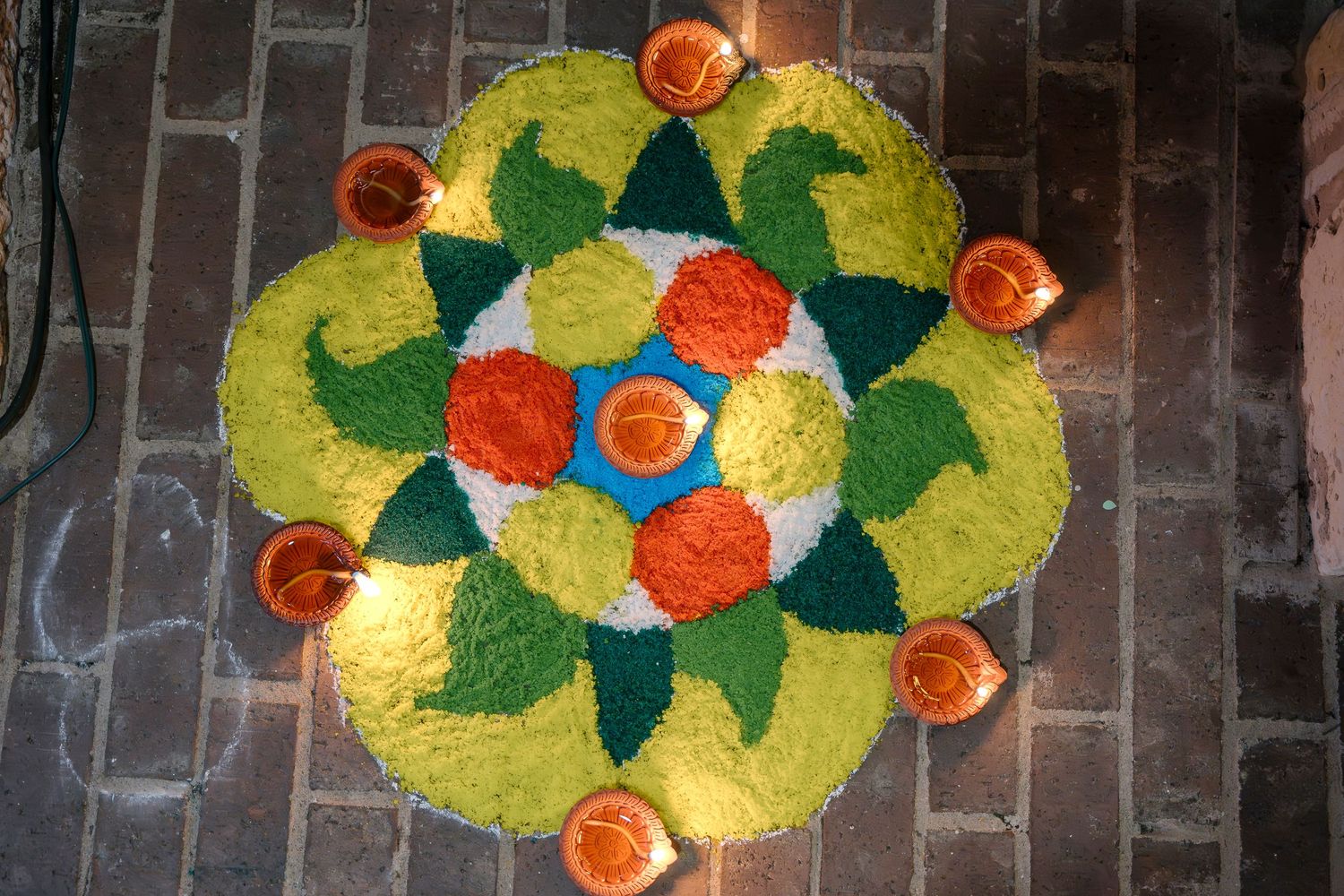 Traditional floral rangoli pattern decorated with orange diyas in a circular formation.