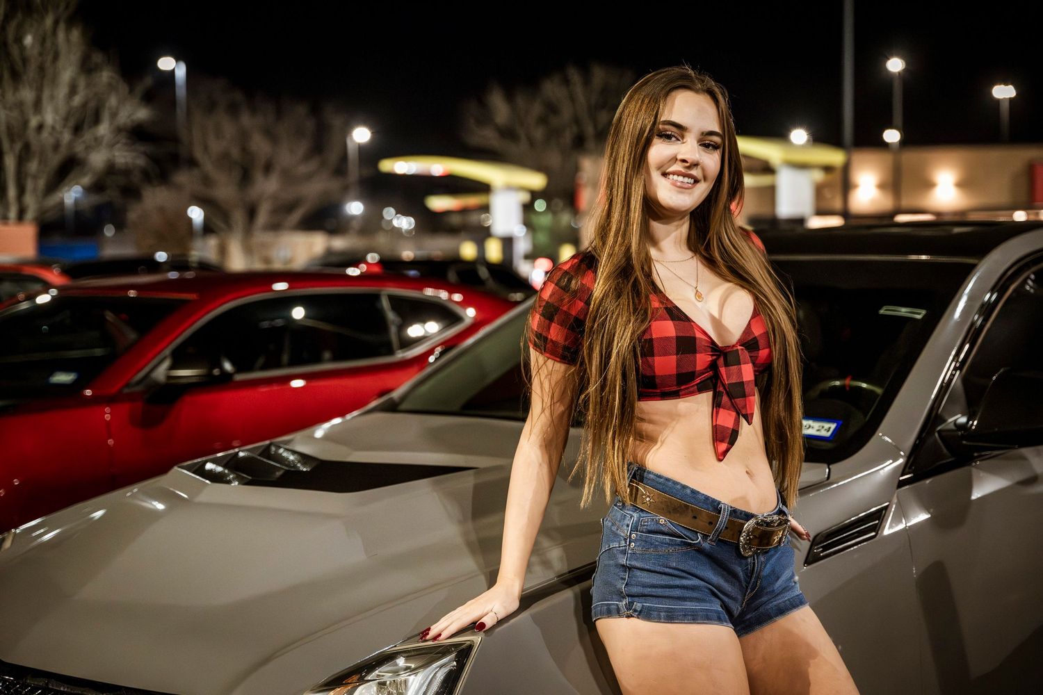 Person leaning against car in parking lot at night.