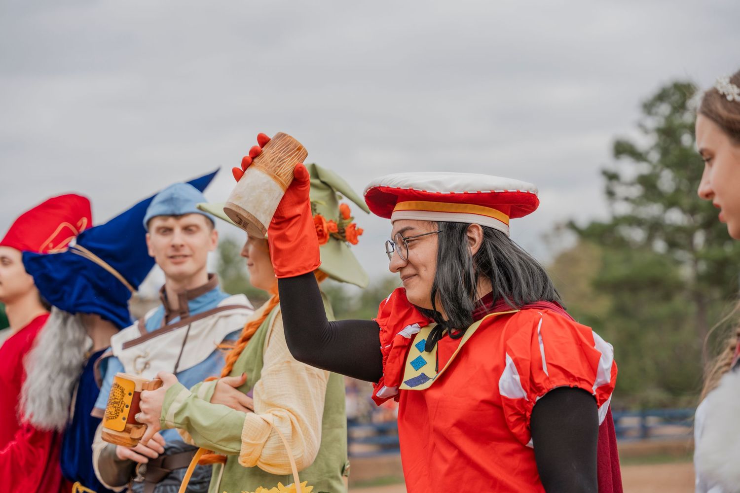 Festival performers in vibrant medieval costumes raising their arms during an outdoor performance.