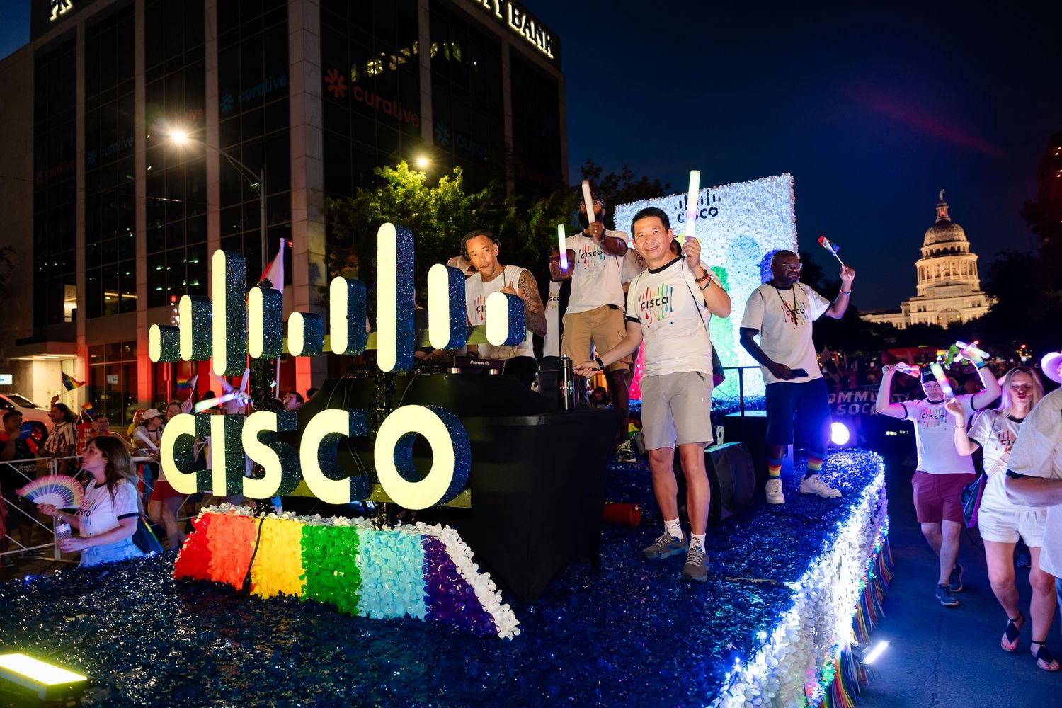 Cisco-branded float with colorful rainbow decorations at a nighttime Pride parade near a lit government building.