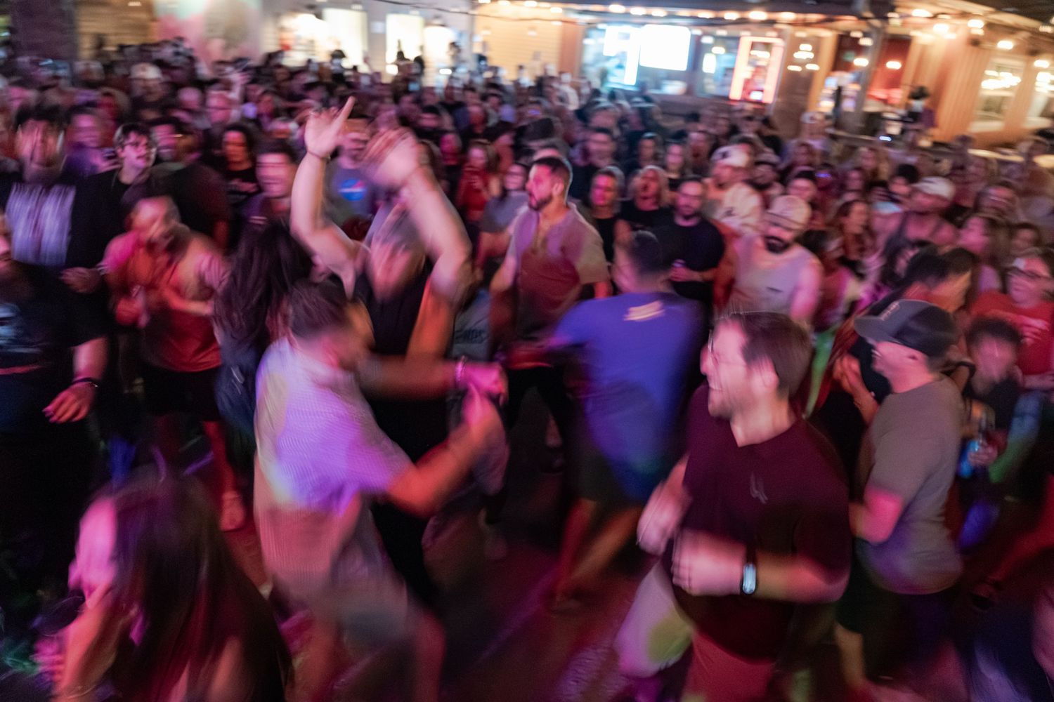Energetic crowd of people dancing at a lively indoor party or concert venue with colorful lighting.